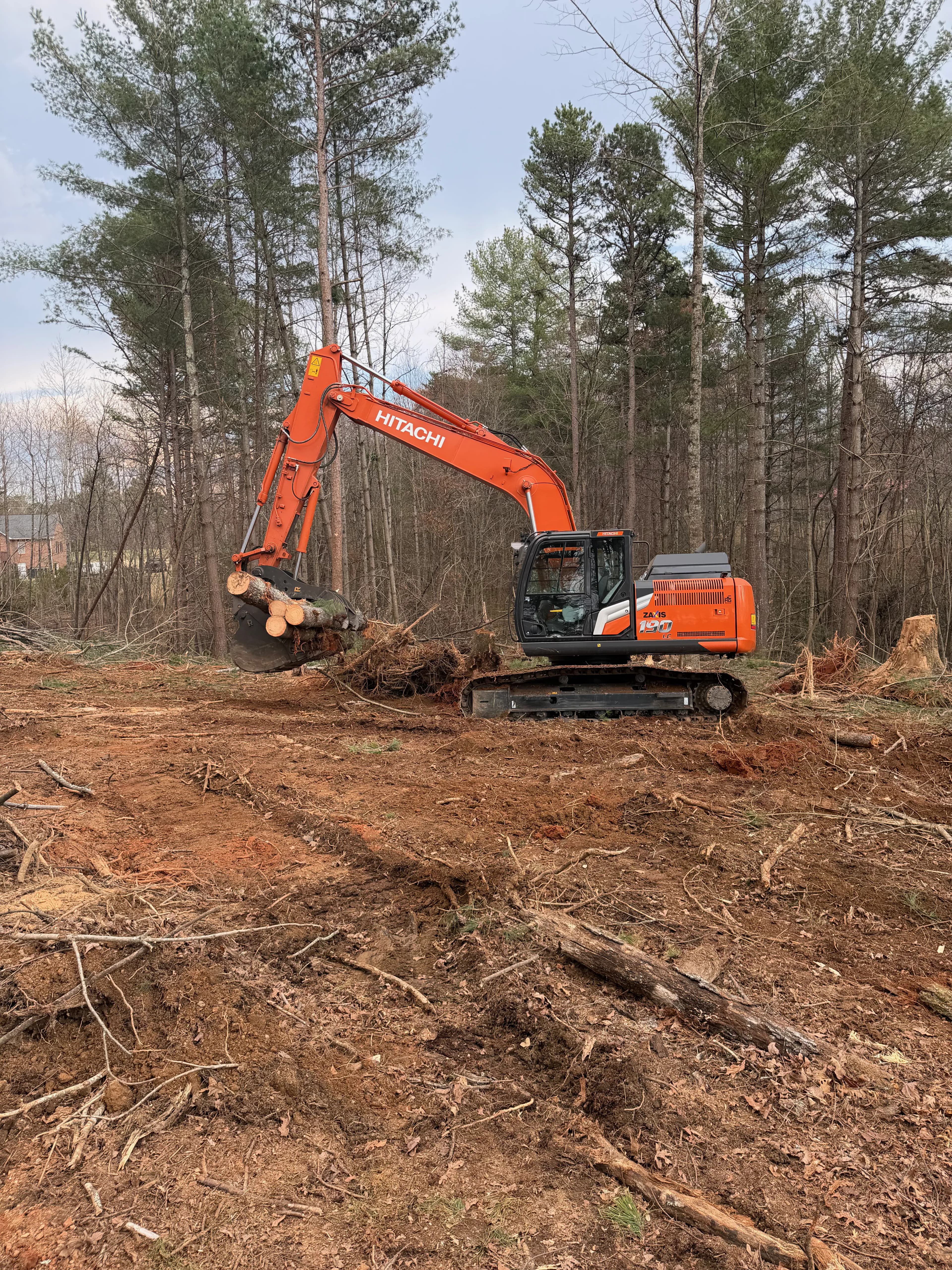 Land Grade Solutions track hoe lifting logs